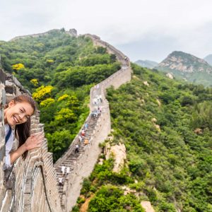 China travel tourist having fun waving hello at the Great Wall in Badaling smiling happy at camera. Woman tourist traveler enjoying her summer vacation holidays in Asia. Multicultural model.